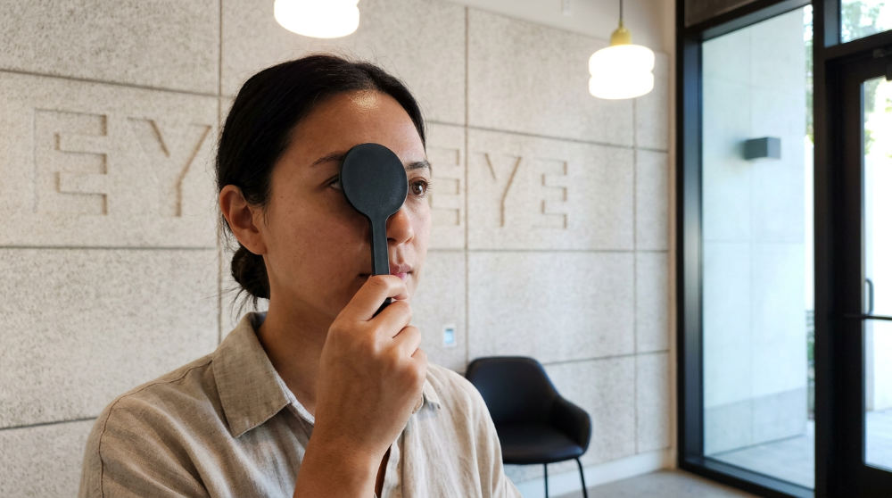 A person performing a home vision screening by covering one eye with an occluder paddle to check their visual acuity.